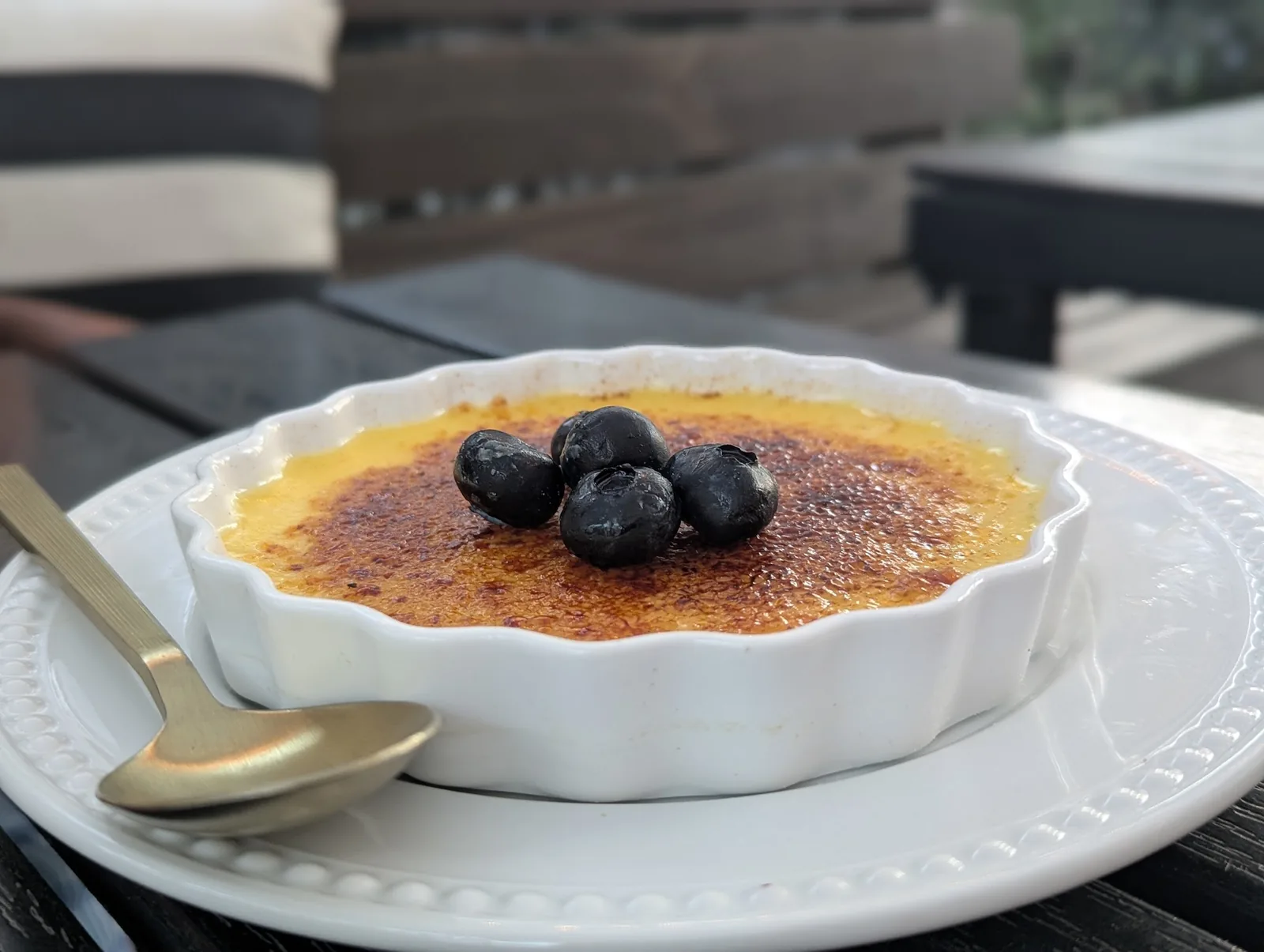 A cr&egrave;me br&ucirc;l&eacute;e topped with blueberries in a white fluted dish