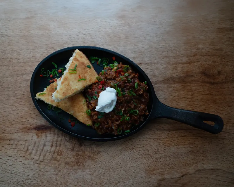 Chilli con carne in a cast-iron skillet with soured cream and flatbread