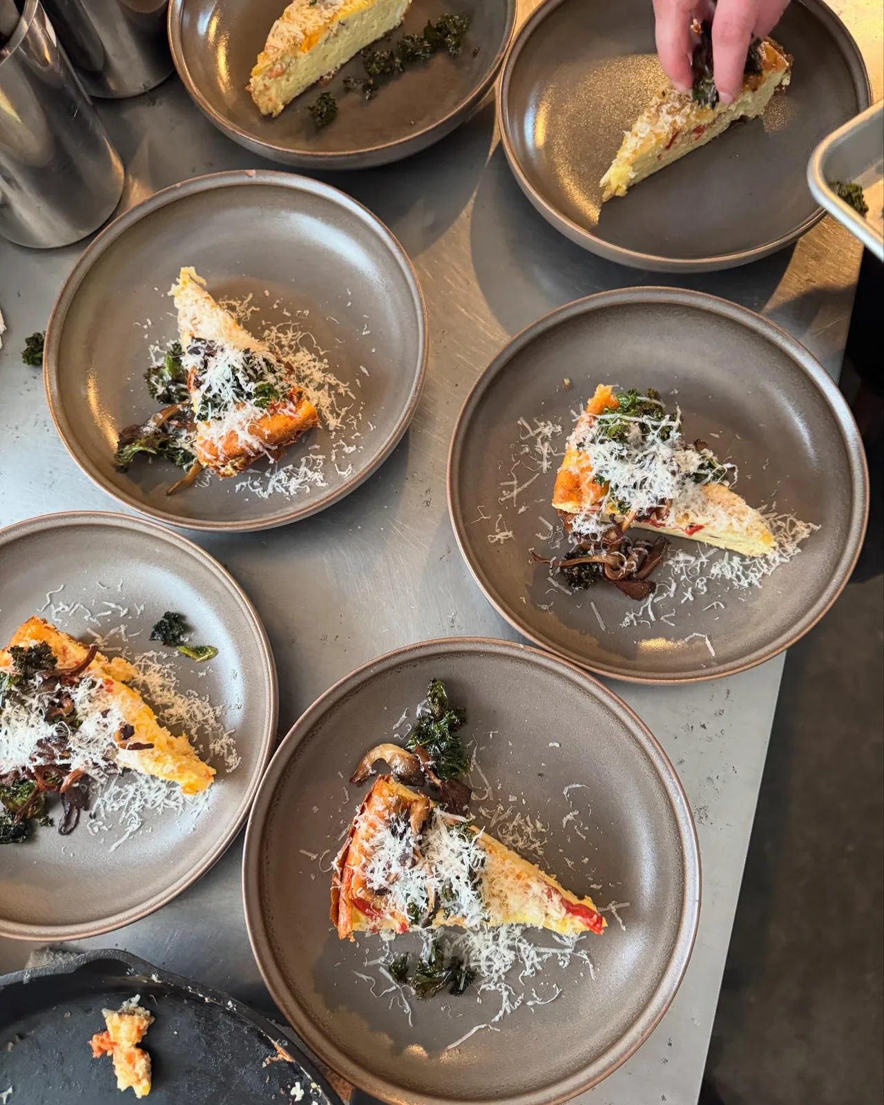 Three identical plated salmon dishes lined up at the pass in the Bistro Ten kitchen
