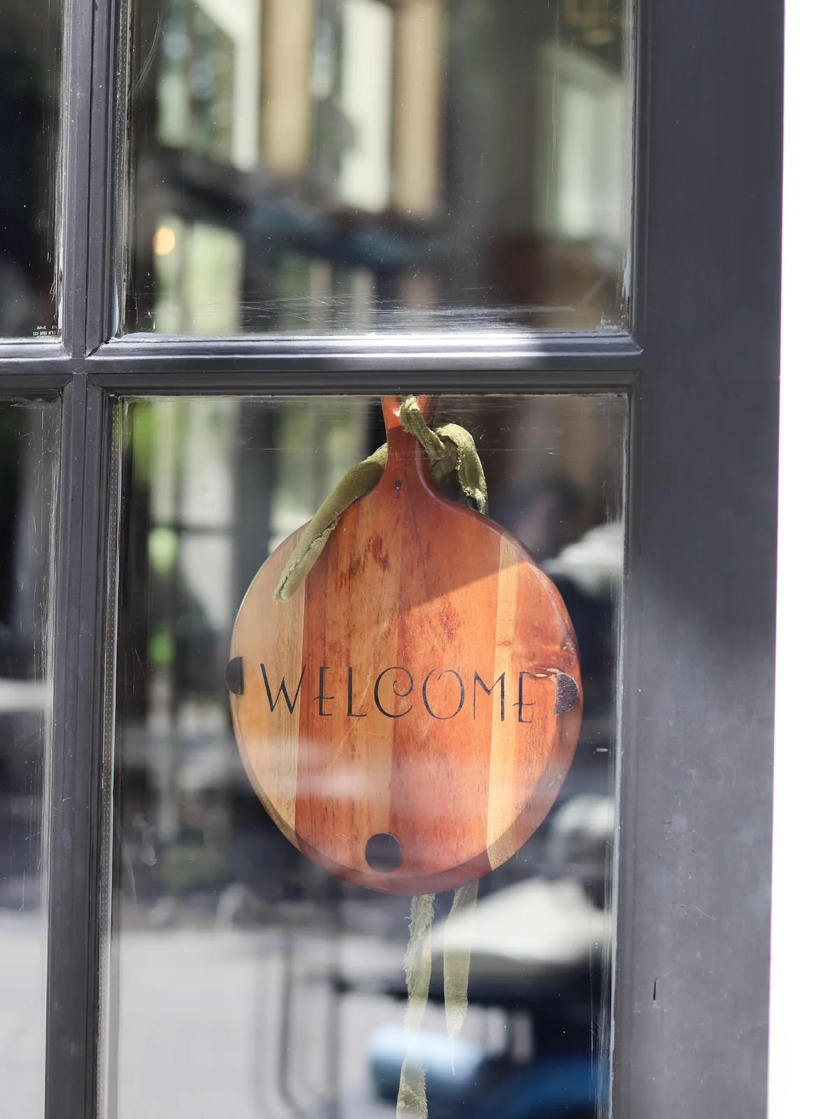 A hand-painted wooden tomato sign reading Welcome, hanging in the window at Bistro Ten